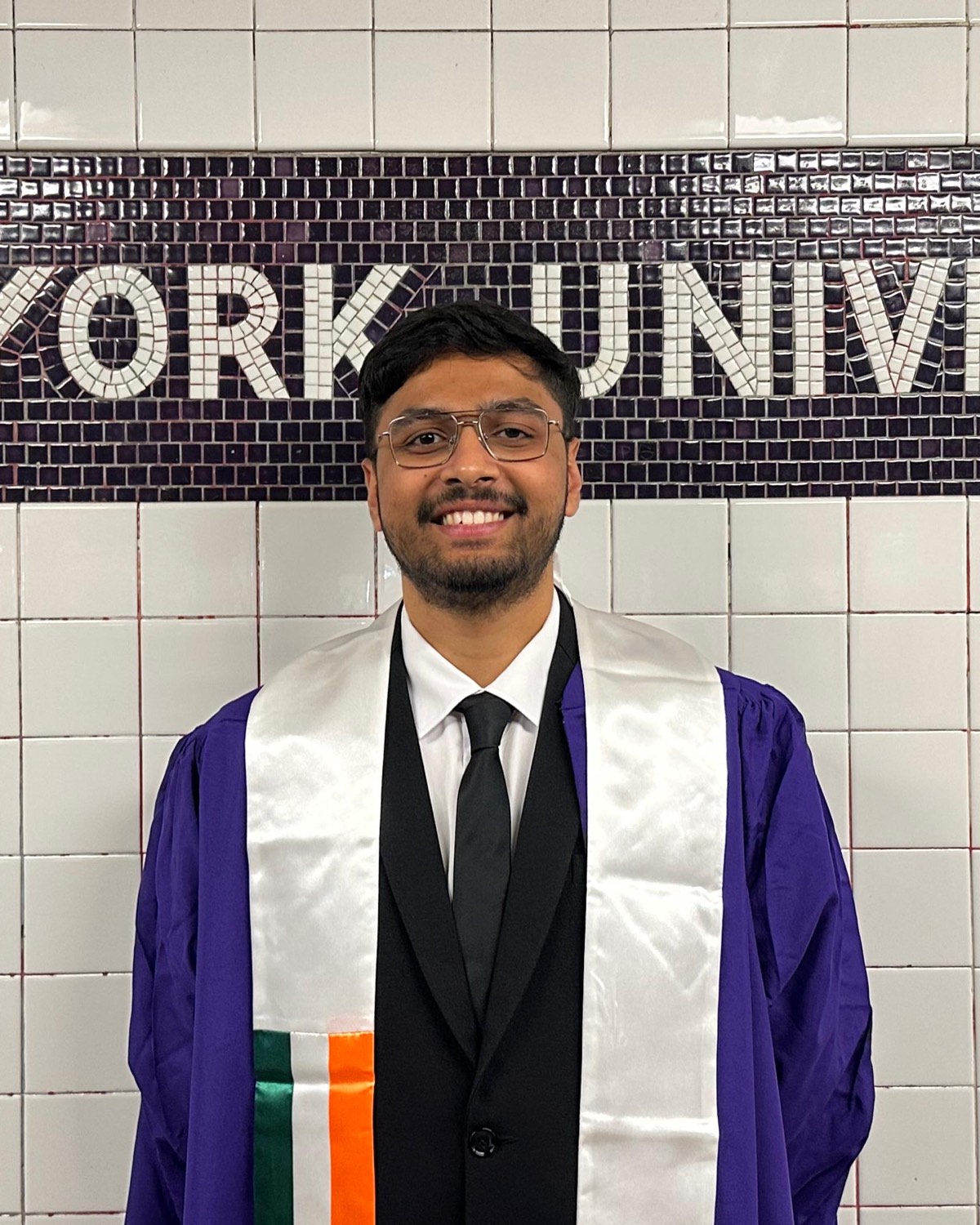 Om Thakur in NYU graduation regalia at the New York University subway mosaic